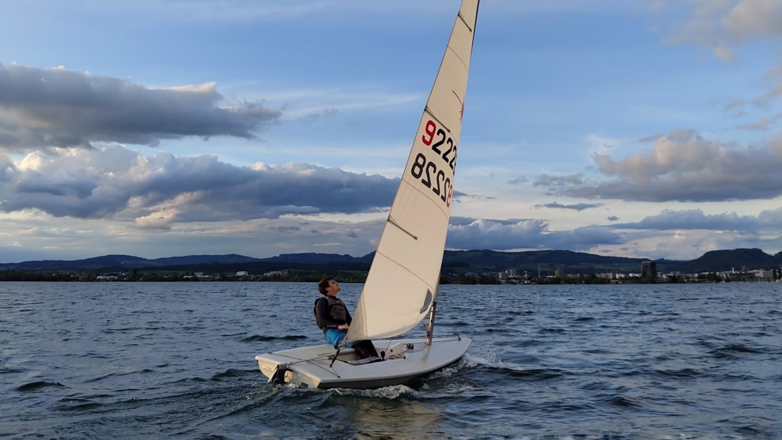 Sailor hiking out in a Laser dinghy to keep the hull perfectly flat, demonstrating the 'Flat is Fast' principle of sailing balance.