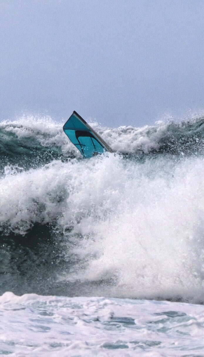 Windsurf sail cutting through rough ocean waves, illustrating the real-world water sports experience behind our coaching approach.