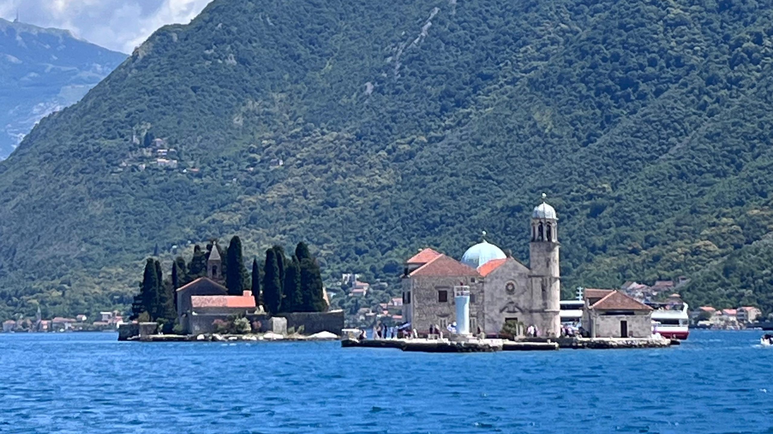 View of Our Lady of the Rocks and St. George islands in the Bay of Kotor, Montenegro, set against a backdrop of steep, green mountains.